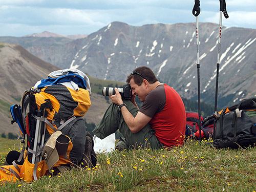 Todd Egan sitting at the top of a mountain with camera and hiking gear